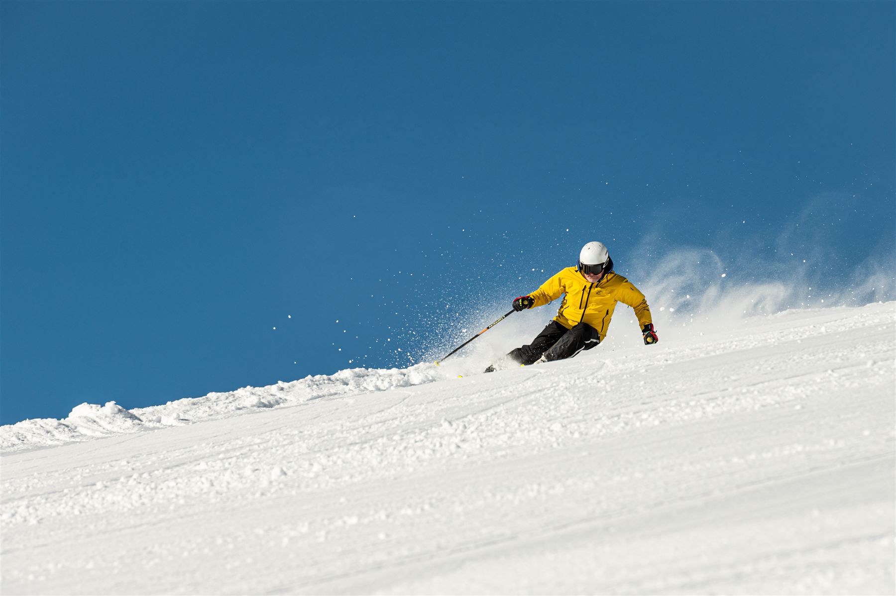 Sciatore in maglia gialla in piega con la neve alzata
